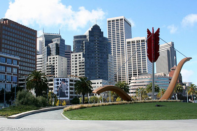 A metal sculpture of a large bow and arrow on the grass, with a view of San Francisco downtown in the background.