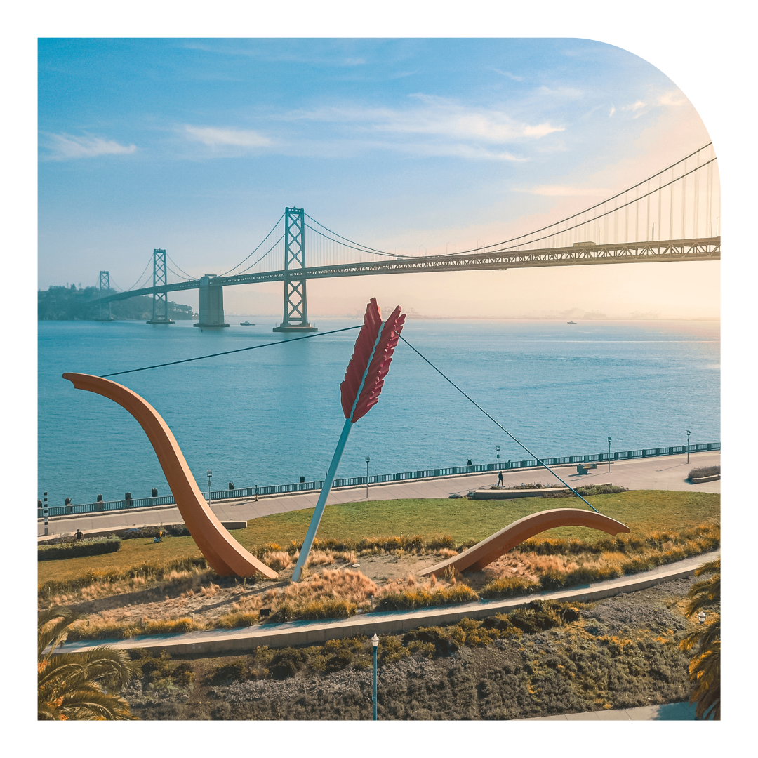 photo of large arrow sculpture with the Bay Bridge in the background