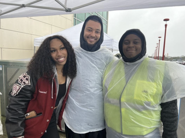 Three people stand in rain gear to distribute food
