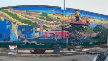 Man on lift painting a colorful mural of the city in pastel colors