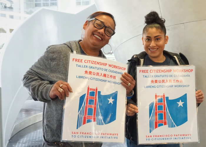 Two volunteers hold signs leading people to a free citizenship workshop in the library