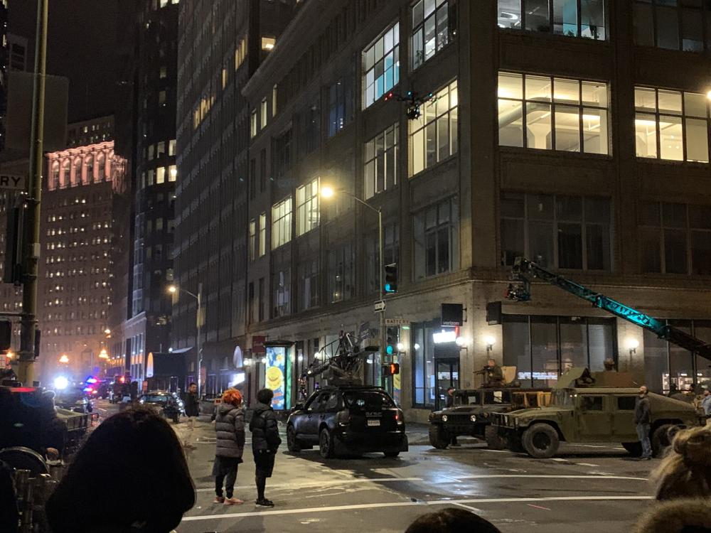 Two prop military vehicles face a car holding up a large camera rig on Battery Street at night, overseen by the orange-haired director Lana Wachowski.