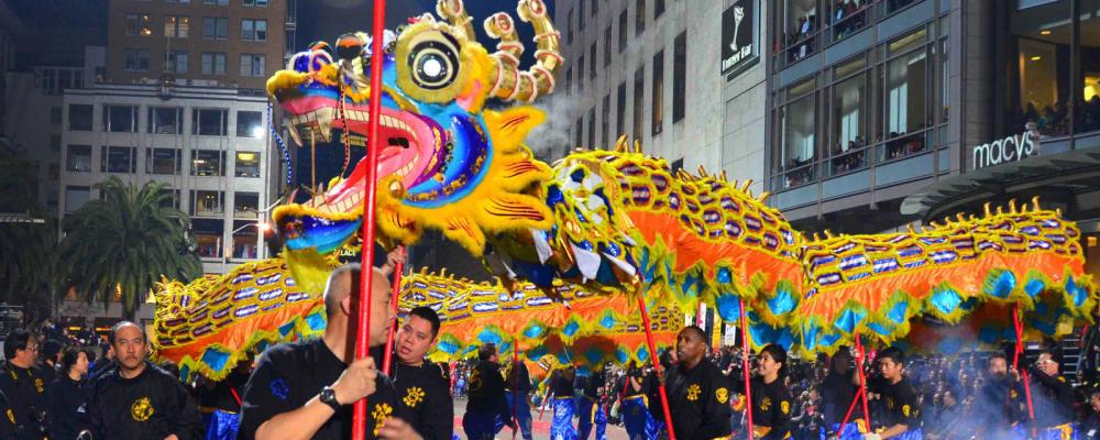 A line of performers wearing black t-shirts hold a large, colorful dragon over their heads during the Lunar New Year Parade.