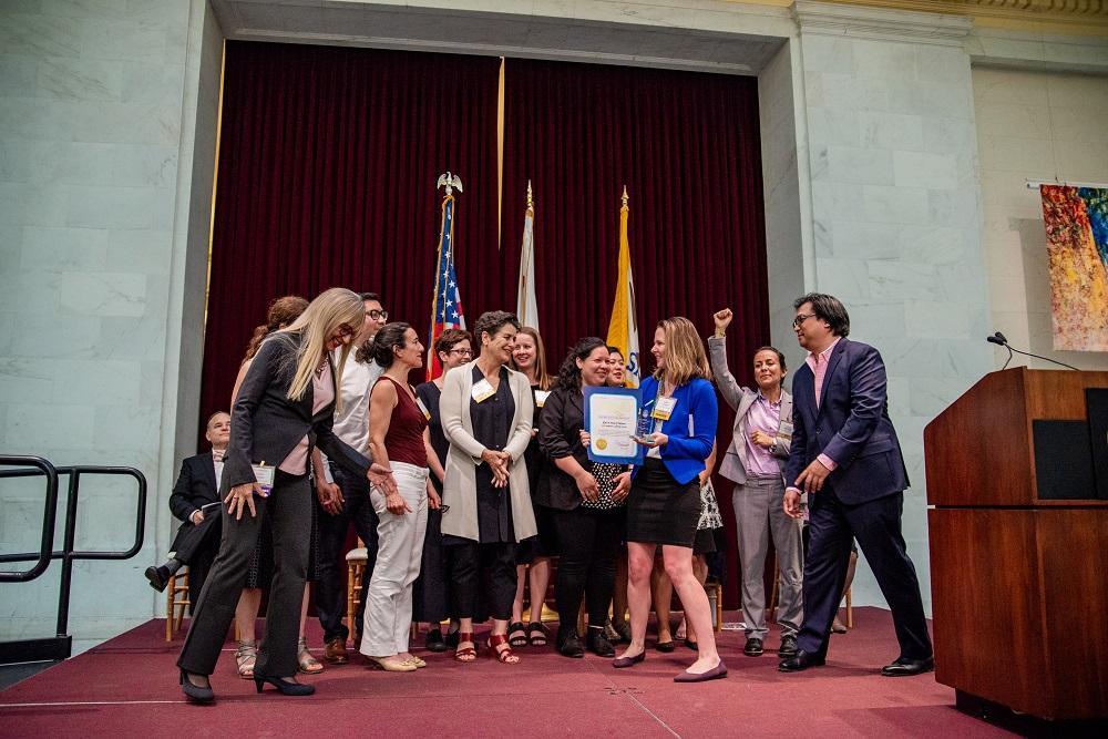 A group celebrates receiving the Immigrant Leadership Award on stage at City Hall
