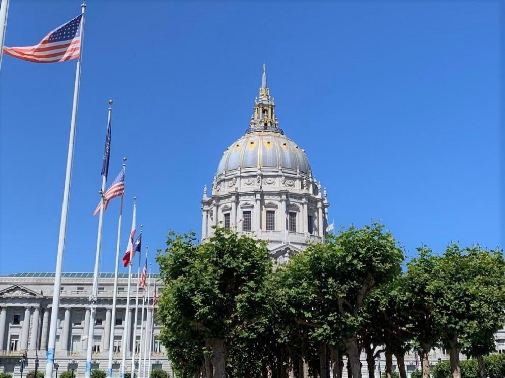 Image of San Francisco City Hall with flag poles and trees in foreground