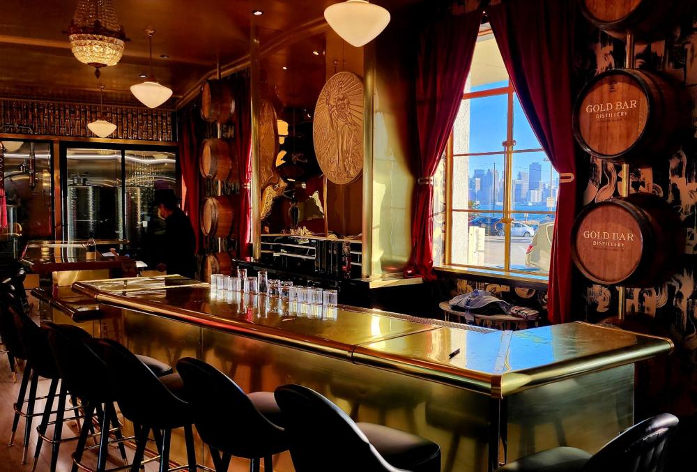 The Goldbar tasting room on Treasure Island is shown, there are seats and tables and a bar andand a view of San Francisco