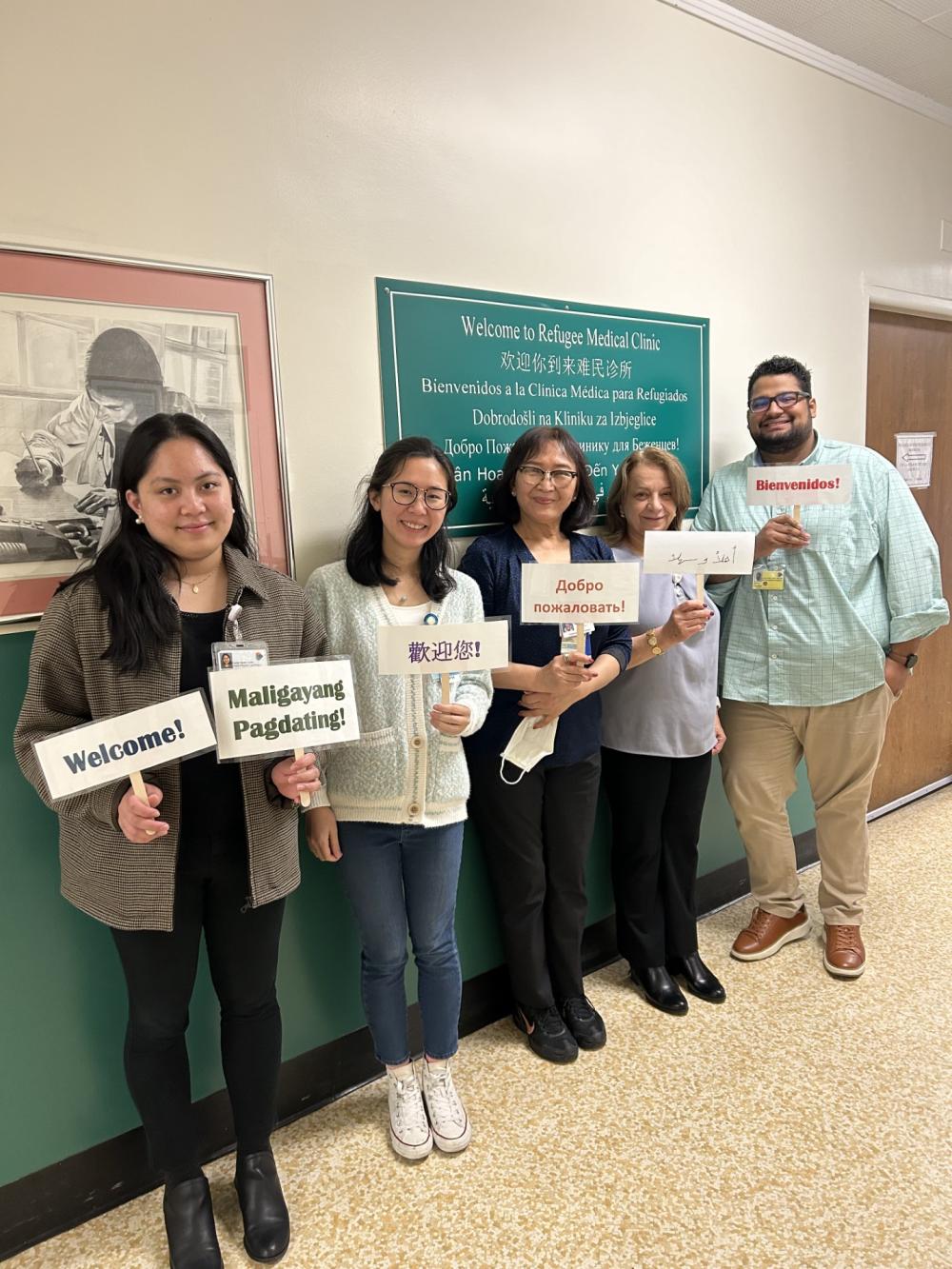 Newcomers Health Program team members holding "Welcome" signs in various languages, posing in front of sign at the Family Health Center's Refugee Medical Clinic